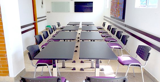 Sala L con mesas en formato de clase y sillas moradas