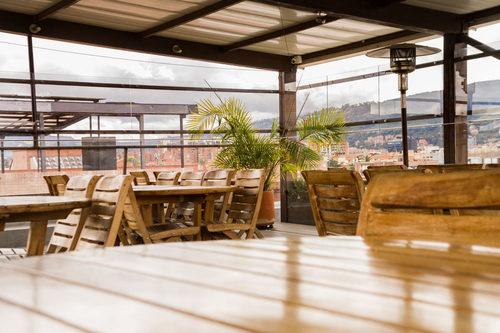 Terraza cubierta con mesas de madera y vista a los cerros
